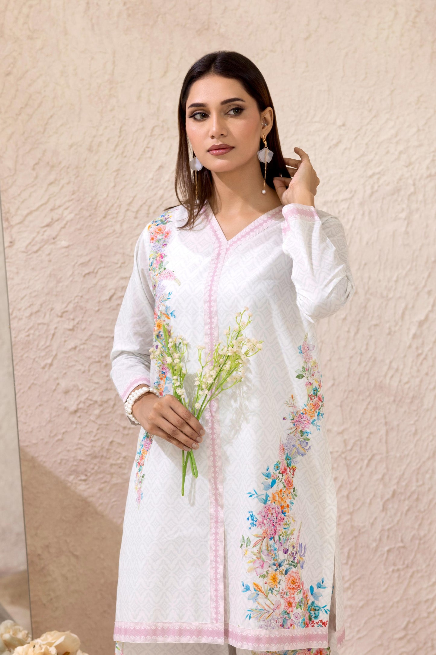 Woman wearing a white embroidered outfit holding flowers against a light background